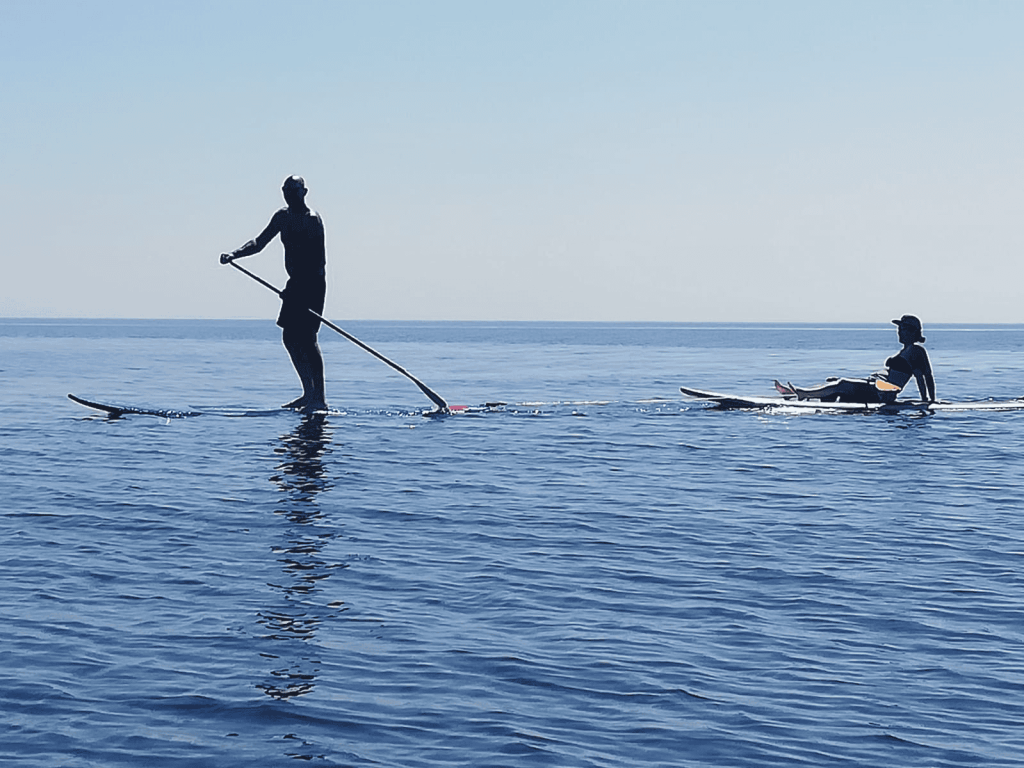 A man and a woman riding a surfboard together, enjoying the waves and sunshine on a beautiful day at the beach.