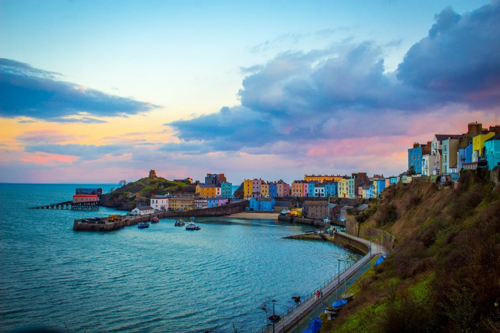 Beautiful view of Tenby at sunset, with colorful clouds illuminating the sky and seaside houses along the coastline, creating a picturesque and serene scene.