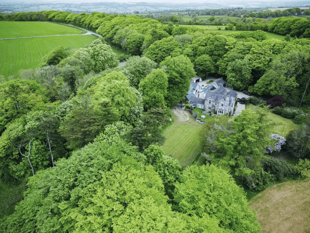 Aerial view of Hill House Country Estate surrounded by lush green trees and open fields in a rural landscape.