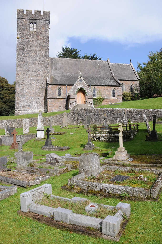 Historic stone church with tall tower and arched entrance, surrounded by old gravestones in a green churchyard.