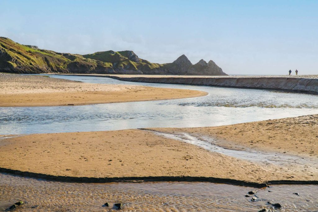 A winding river flows through a sandy beach, with cliffs visible in the background.