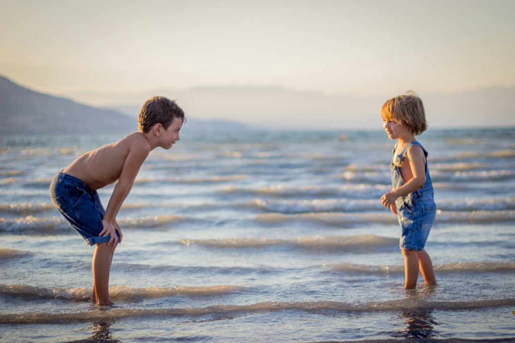 Two boys having fun in the water at the beach, laughing and splashing as they play under the sun.