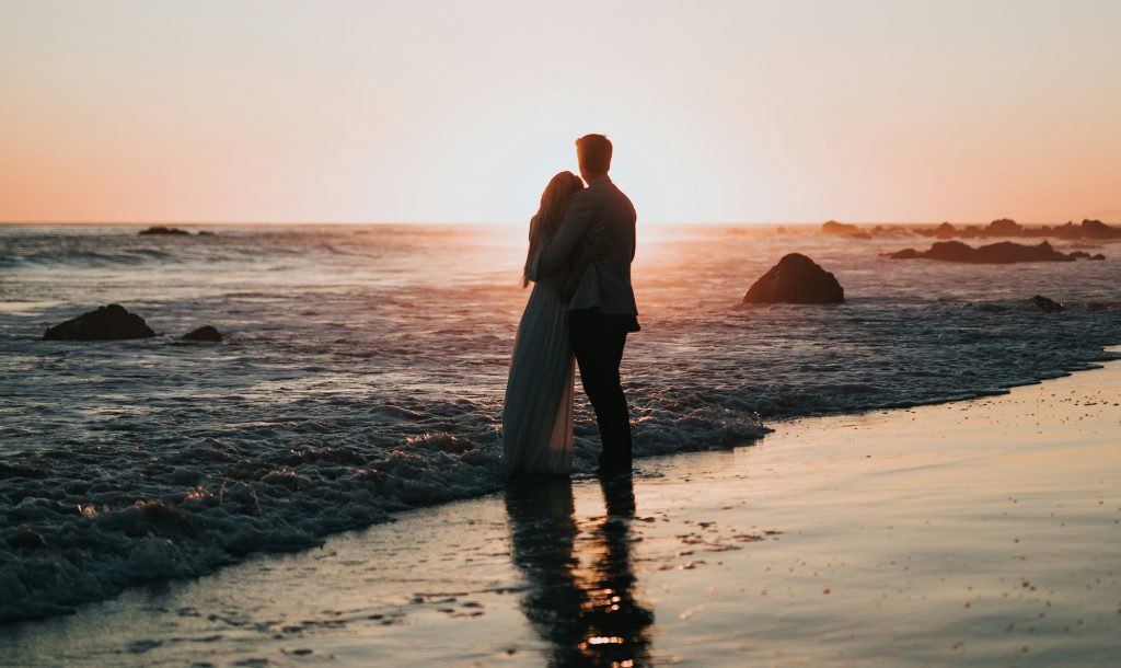 A romantic scene of a couple enjoying a sunset stroll along the beach, with waves gently lapping at their fee