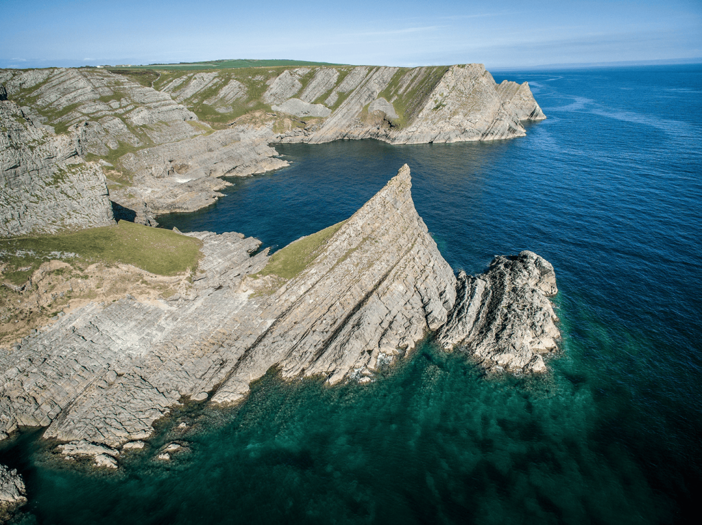 Aerial view showcasing the stunning cliffs along the coast of Wales, with waves crashing below.